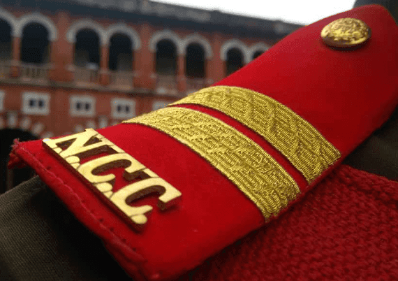 NCC shoulder badge on uniform with Anna University Red building in the background